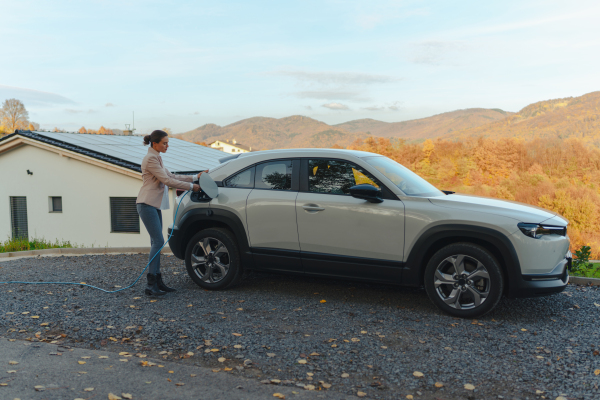 Young woman chargingher car in home, sustainable and economic transportation concept.