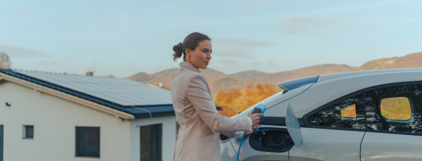 Young woman chargingher car in home, sustainable and economic transportation concept.