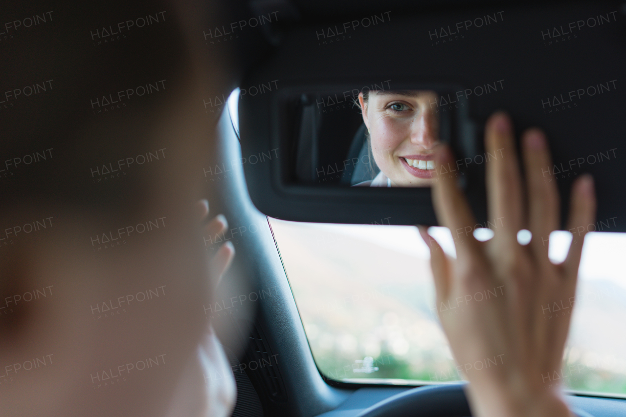 Rear view of young woman in car, looking at a rearview mirror.