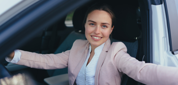 Excited young woman sitting in her car, prepared for a drive.