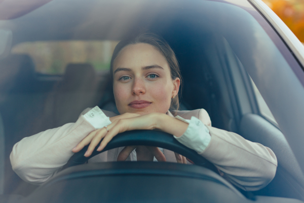 Excited young woman sitting in her car, prepared for a drive.