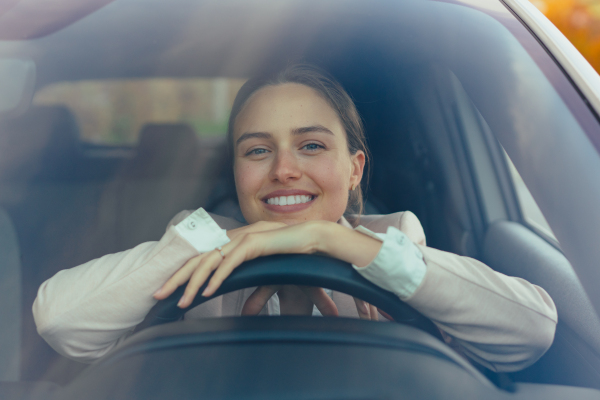 Excited young woman sitting in her car, prepared for a drive.