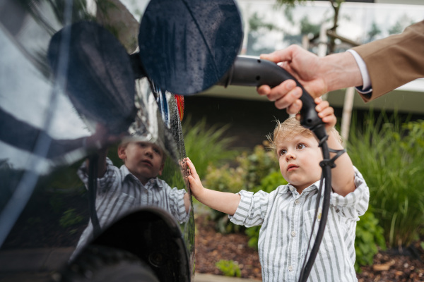 Close up of man and his little son charging the electric car.