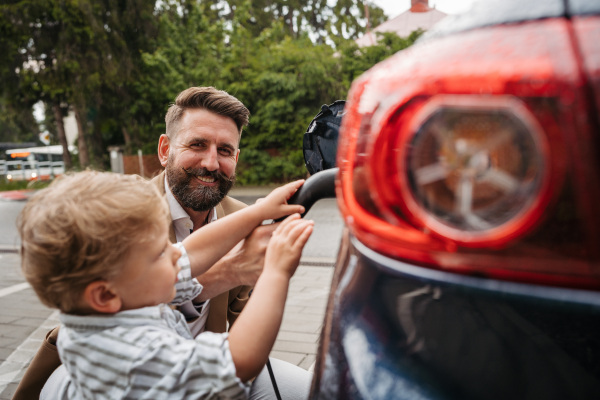 Father and his little son charging their electric car on the street. Cute little boy helping dad to plug in charger in charging port.