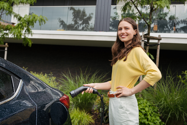 Close up of beautiful woman plugging charger in her electric car. Progressive woman charging her electric car on the street. Pluging in charger in charging port.