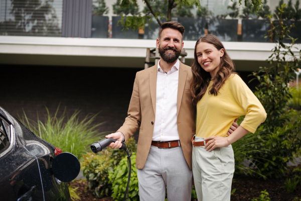 Happy young couple charging their electric car on the street. Future parents choosing electric vehicle as a family car.