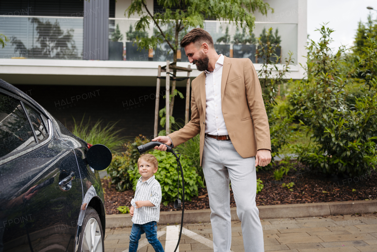 Smiling father and his little son charging their electric car on the street. Cute boy lookign at dad, learning how to plug in charger in charging port.