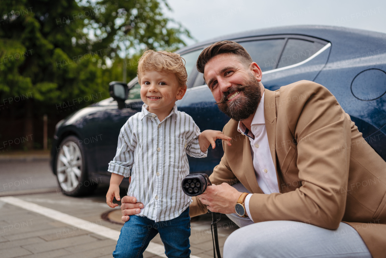 Close up of man and his little son holding a power supply cable from their electric car.