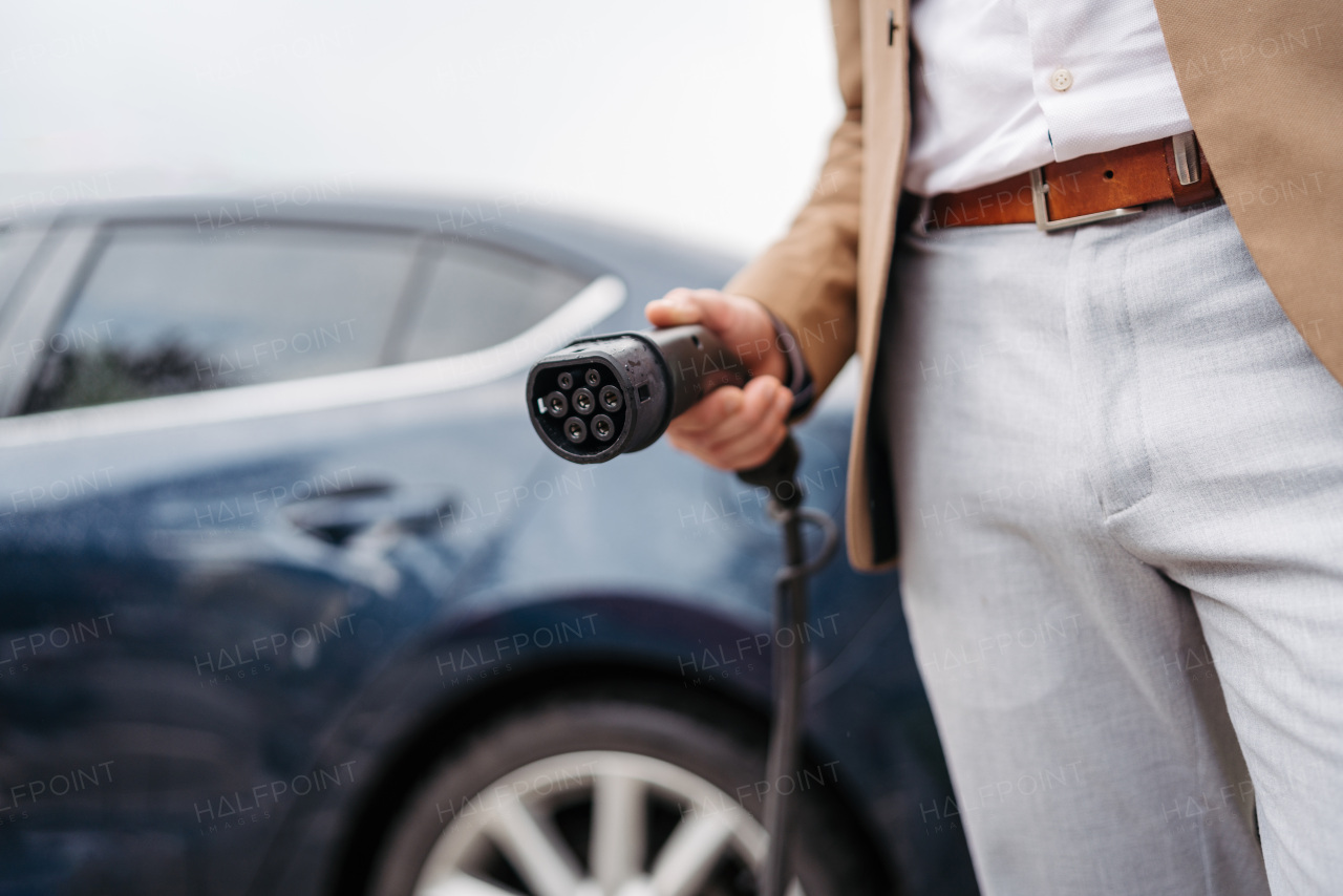 Close up of businessman charging electric car.