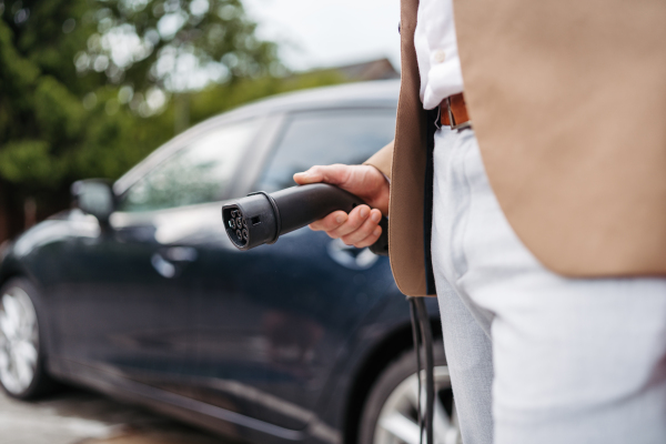 Close up of a businessman holding electric charger for electric car. An electric vehicle charging station.