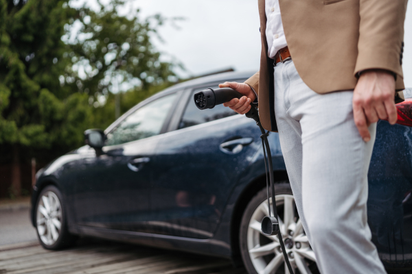 Close up of businessman charging electric car, holding power supply cable.