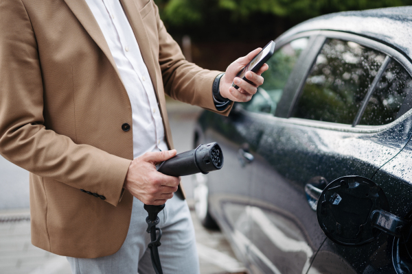 Close up of a businessman holding electric charger for electric car. An electric vehicle charging station.