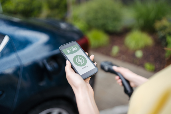 Close up of woman using electric vehicle charging app, checking charging of electric car from smart phone. Charging apps for monitoring electricity usage, locating charging stations.