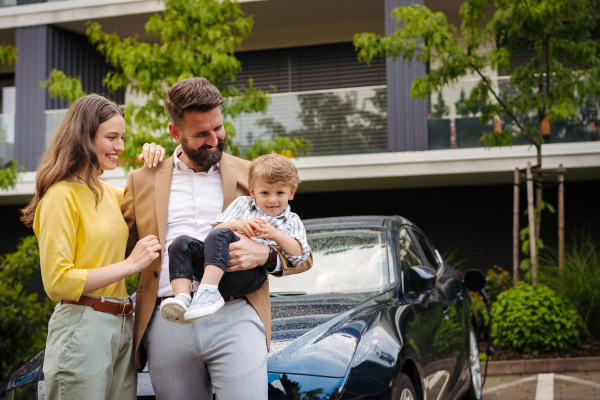 Happy family standing in front their electric car and charging it on the street. Electric vehicle with charger in charging port.