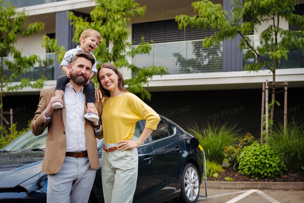 Happy young family with little son waiting for charging the electric car.