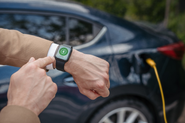 Close up of businessman with smartwatch, checking charging of the electric car.