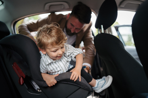 Young father gvinig his little son in a car seat.