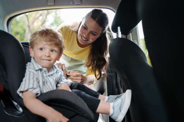 Young mother putting little son in a car seat. Buckling toddler into child safety seat properly.