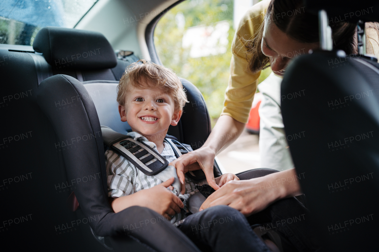 Young mother putting little son in a car seat. Buckling toddler into child safety seat properly.