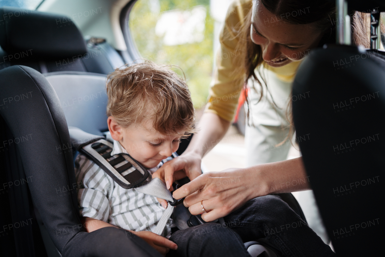 Young mother putting little son in a car seat. Buckling toddler into child safety seat properly.