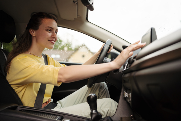 Young woman touching multimedia touch screen in her car. Woman connecting her phone with car. Businesswoman using navigation system while driving to a meeting.