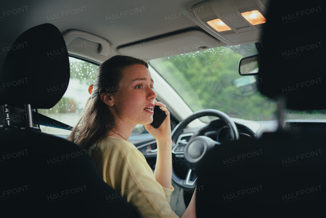 Scared woman sitting in electric car with drained battery, making a phone call to the service center. Woman with broken down car calling for help.