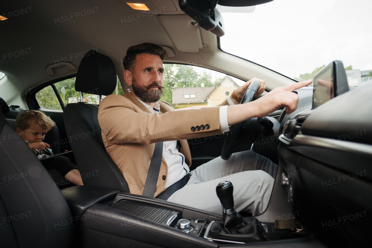 Young man touching multimedia touch screen in car. Man connecting his phone with car. Businessman using navigation system while driving to a meeting.