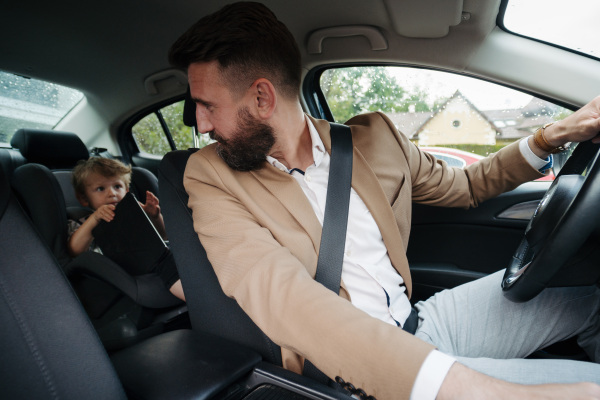 Young man sitting in his new car with little son, prepared for a ride.