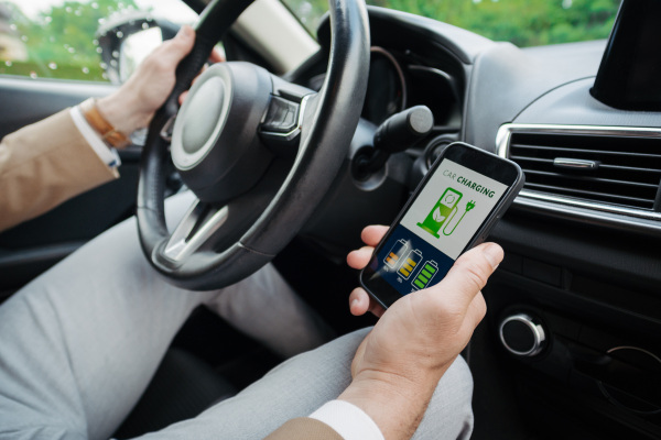 Close up of businessman using electric vehicle charging app, checking electricity usage and the nearest charging station from his smart phone.