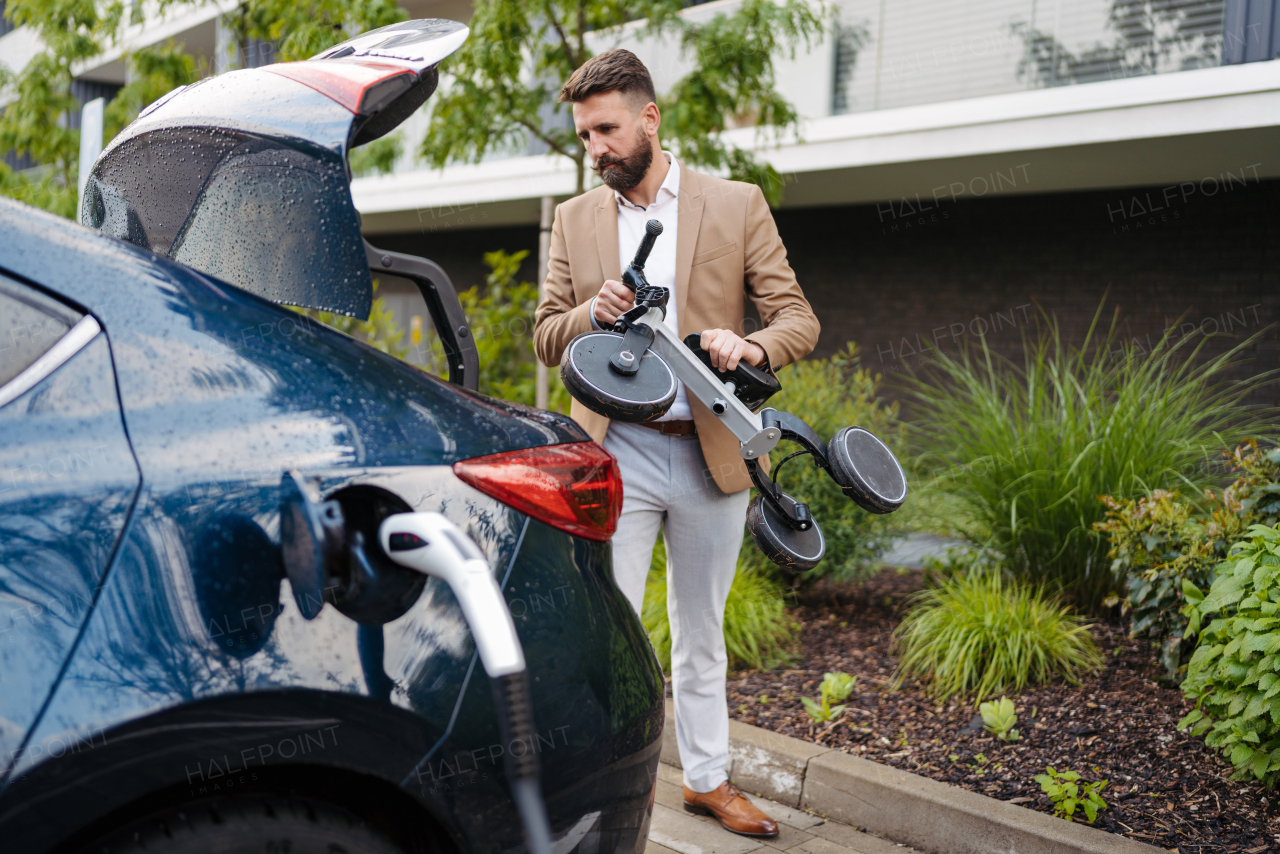 Handsome man loading children bike into a car trunk. Working father taking his son to the park after work day. Getting ready for a trip, while charging electric car.