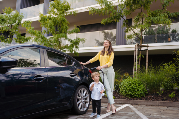 Smiling mother and her little son charging their electric car on the street. Cute boy holding model of wind turbine.