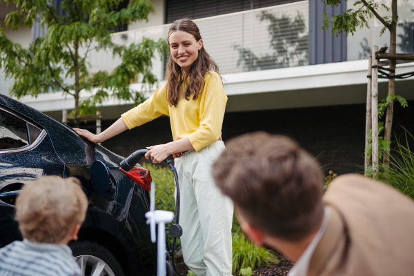 Happy young family with little son waiting for charging the electric car.