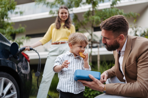 Happy young family with little son waiting for charging the electric car.