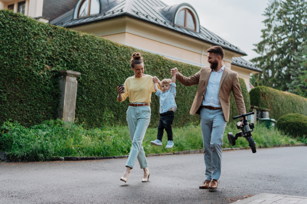 Young family with little son on a walk in a city park after work. Working parents spending time with their son after work day. Parents pick up kid from daycare.