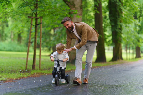 Single father teaching his little son how to bike in public park. Working parent spending time with son after work day.