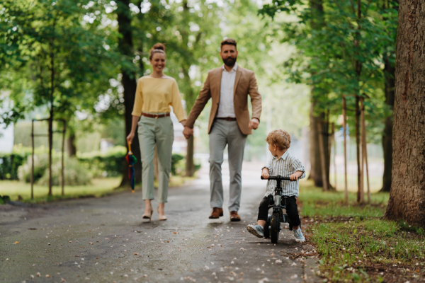 Young family with little son on a walk in a city park after work. Working parents spending time with their son after work day. Parents pick up kid from daycare.