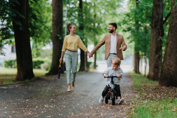 Young family with little son on a walk in a city park after work. Working parents spending time with their son after work day. Parents pick up kid from daycare.