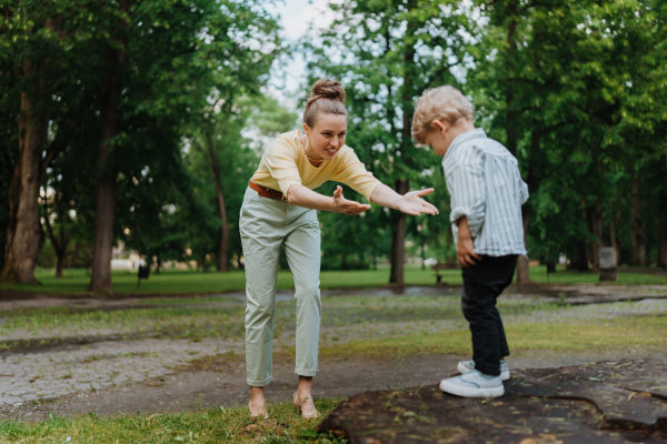 Mom waiting to catch her playful son. A little boy going to jump from tree stump in the park, his mother catches him.