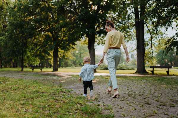 Rear view of mother with little son on a walk after work. Working mother picking up her son from daycare.