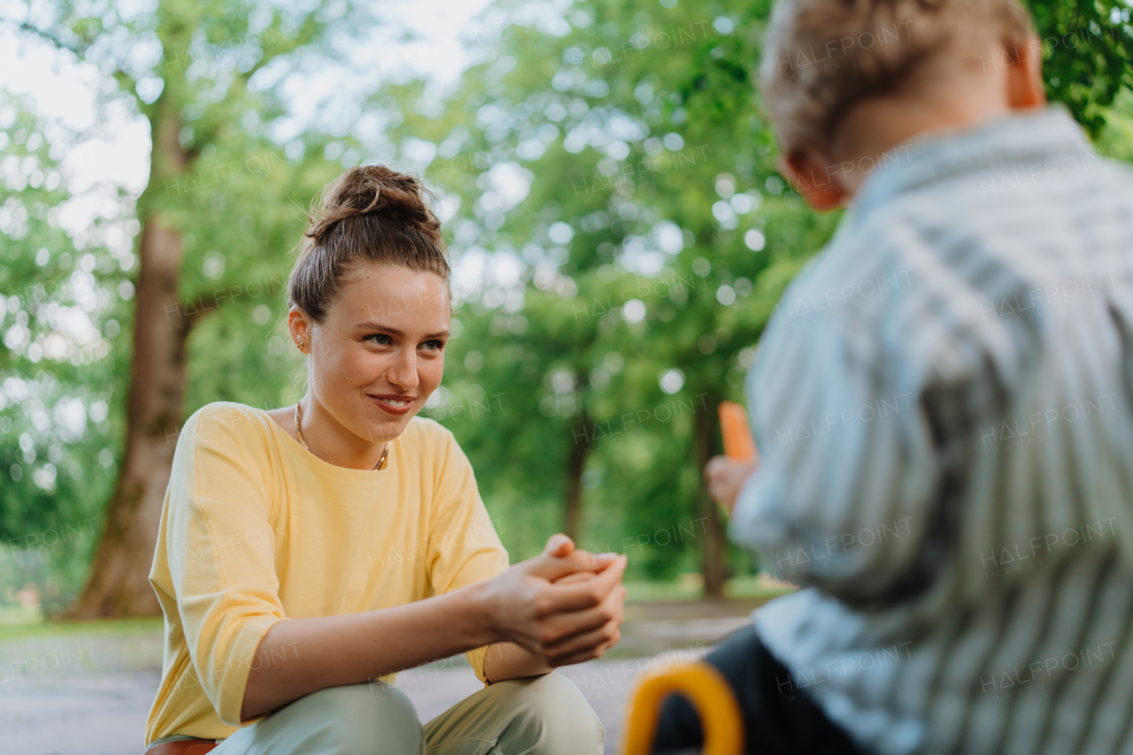 Mother feeding her son with healty snack in a park. Pieces of raw chopped carrots and apricots in lunch box. Eating outdoors on a park bench.