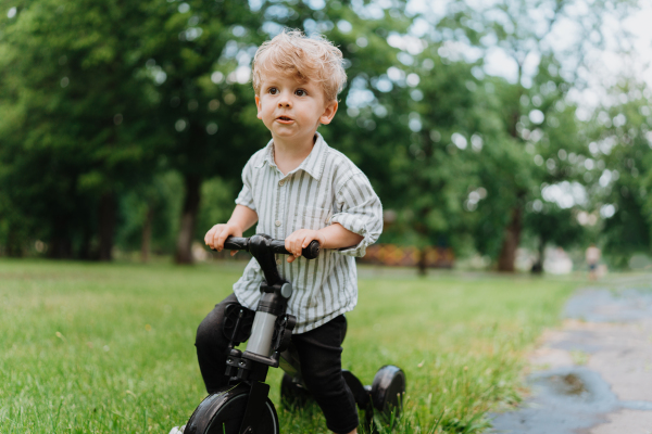 Preschooler playing in the city park, in the fresh air, after finishing kindergarten. Little cute boy riding a scooter in the park.