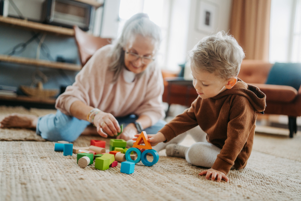 Grandmother playing with her little grandson, building a block set in his room.