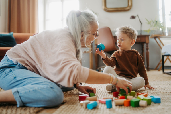 Grandmother playing with her little grandson, building a wooden block set in his room.