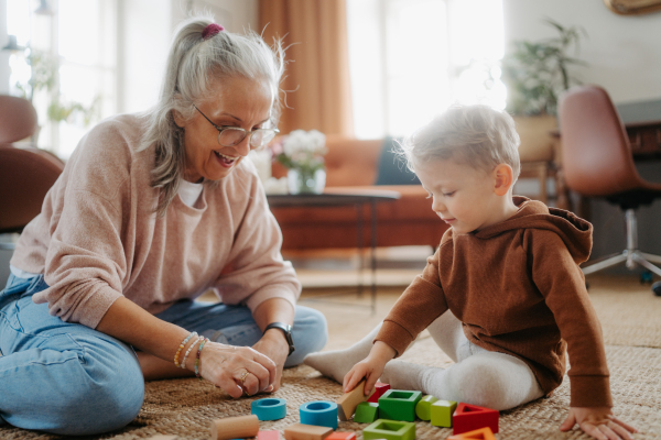 Grandmother playing with her little grandson, building a block set in his room.