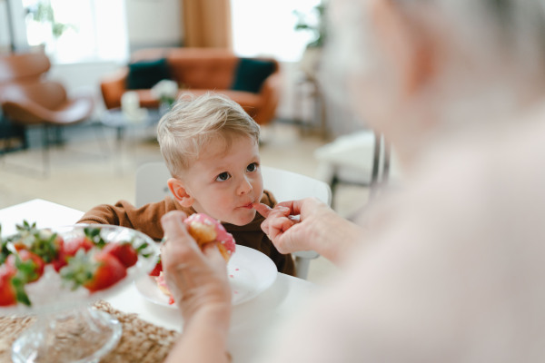 Little boy having sweet snack with his grandmother. Grandmother feeding gradson with donut.