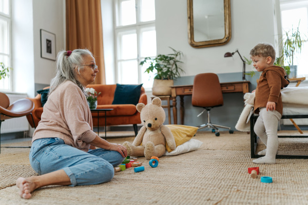 Grandmother playing with her little grandson, building a wooden block set in his room.