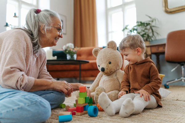 Grandmother playing with her little grandson and teddy bear. Playing with colorful wooden blocks.