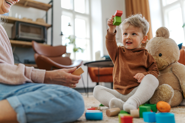 Grandmother playing with her little grandson, building a block set in his room.