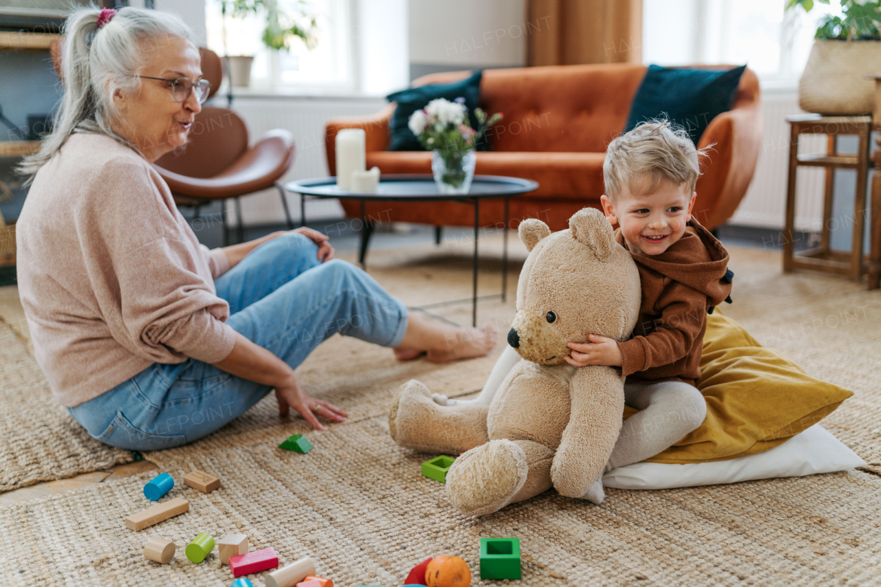 Grandmother playing with her little grandson and teddy bear. Playing with colorful wooden blocks.