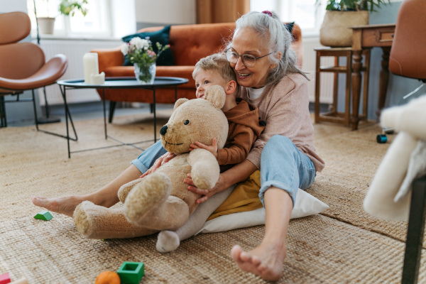 Grandmother cuddling her little grandson with a bear toy.